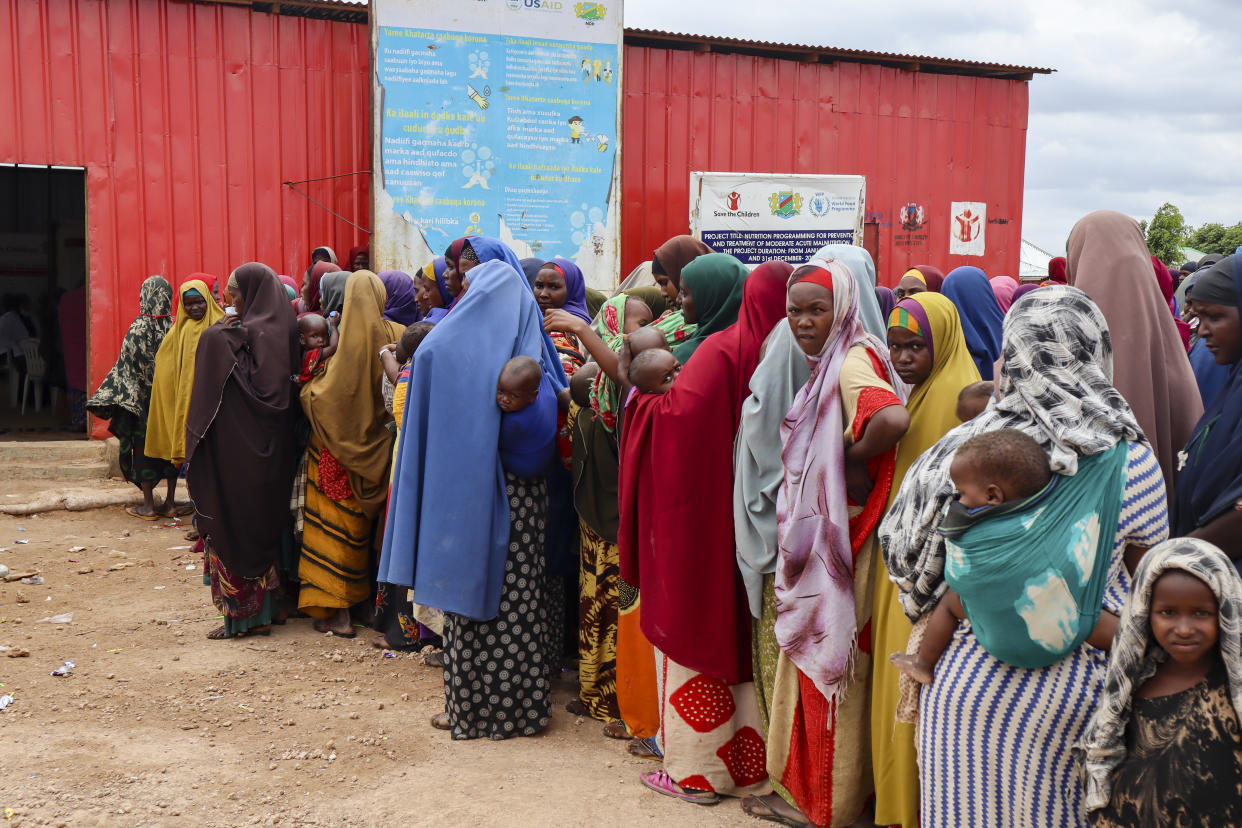 Several lines of Somali women in bright-colored shawls wait with their infants in slings on their backs.