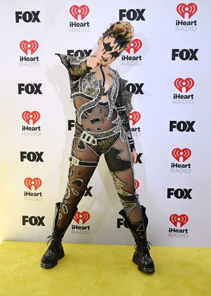 Person posing on red carpet in sparkly bodysuit with cutouts and black boots