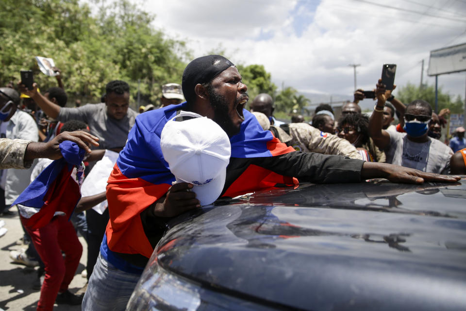 Supporters of former Haitian President Jean-Bertrand Aristide stand in front of a vehicle that is part of the caravan driving him away from the airport after his arrival from Cuba, where he underwent medical treatment, in Port-au-Prince, Haiti, Friday, July 16, 2021. Aristide's return adds a potentially volatile element to an already tense situation in a country facing a power vacuum following the July 7 assassination of President Jovenel Moïse. (AP Photo/Joseph Odelyn)