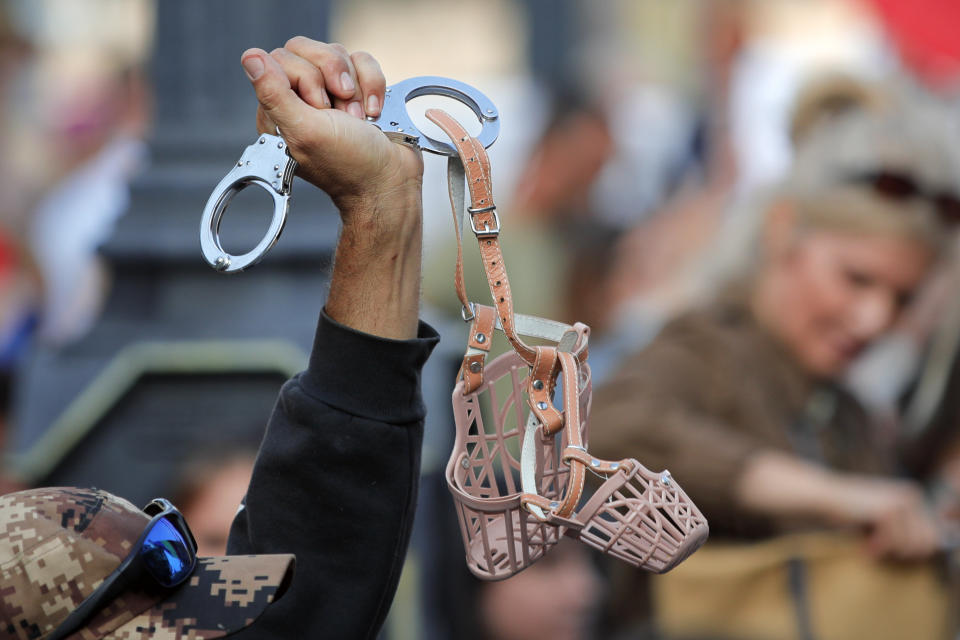 A man waves handcuffs attached to muzzles during a protest in Bucharest, Romania, Saturday, Sept. 19, 2020. Several hundred Romanians, including many families with young children, held a protest in the country's capital against measures meant to curb the spread of the coronavirus, especially social distancing and the mandatory use of masks in schools. (AP Photo/Vadim Ghirda)