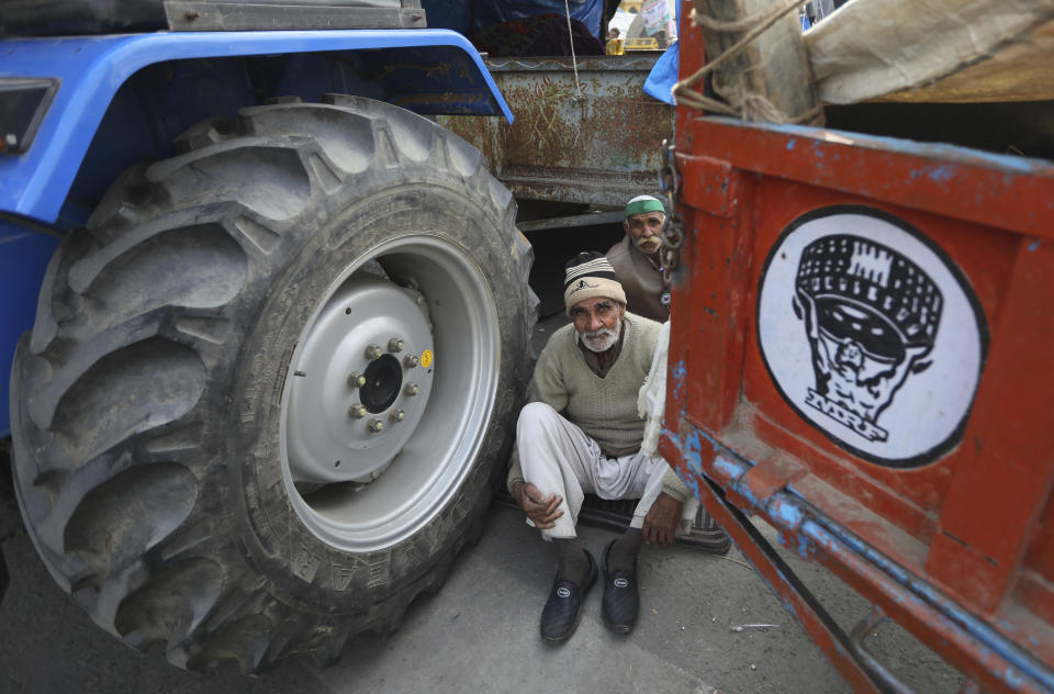 Indian farmers sit near their tractor after arriving at the Delhi-Uttar Pradesh border for Tuesday's tractor rally in New Delhi, India, Monday, Jan. 25, 2021. Thousands of farmers gathered on the borders of Delhi for a massive tractor rally on Tuesday against the three contentious farm laws when India will celebrate its Republic day with a military and cultural parade. The two-month-old old blockade of highways connecting the capital with the country's north continues as the talks have remained deadlocked with the government refusing to scrap the new agricultural reform laws which the farmers say will benefit large corporations. (AP Photo/Manish Swarup)