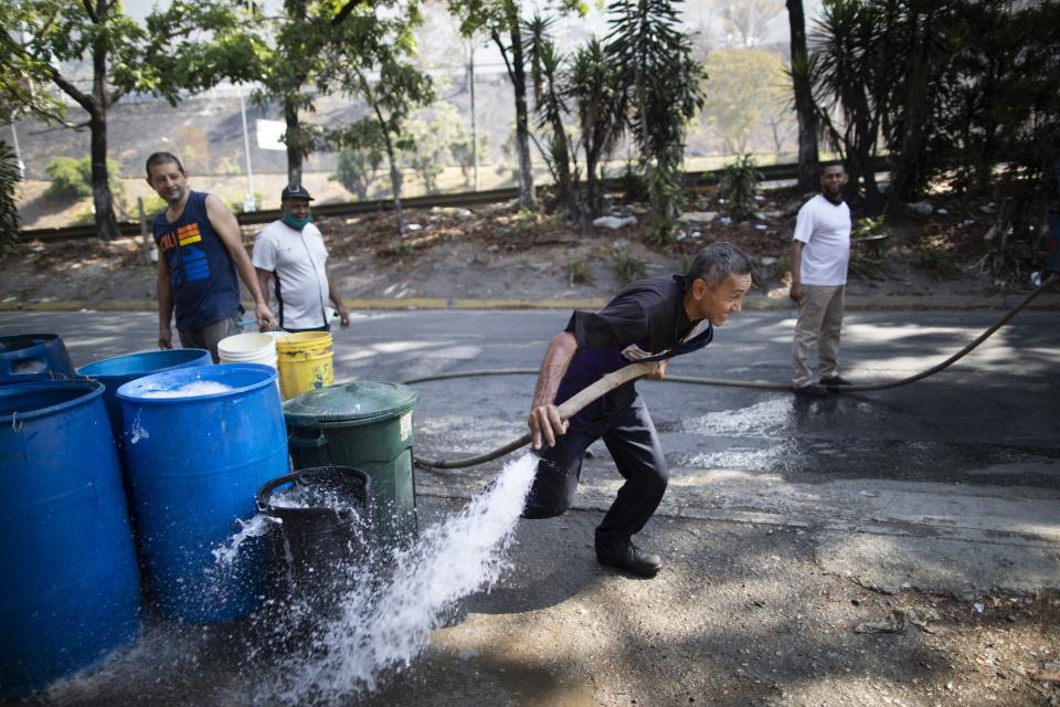 A worker controls a water hose from a government tanker truck to distribute water to residents in the Petare neighborhood of Caracas, Venezuela, Thursday, May 21, 2020. President Nicolas Maduro's government accuses political foes of sabotaging pump stations. As an answer, officials recently celebrated buying a fleet of 1,000 "super tanker" trucks from China to deliver water to residents. (AP Photo/Ariana Cubillos)