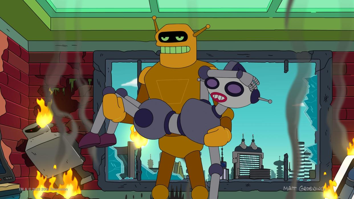  A golden malerobot holds a silver female robot in front of a large window, while fires burn around them. 