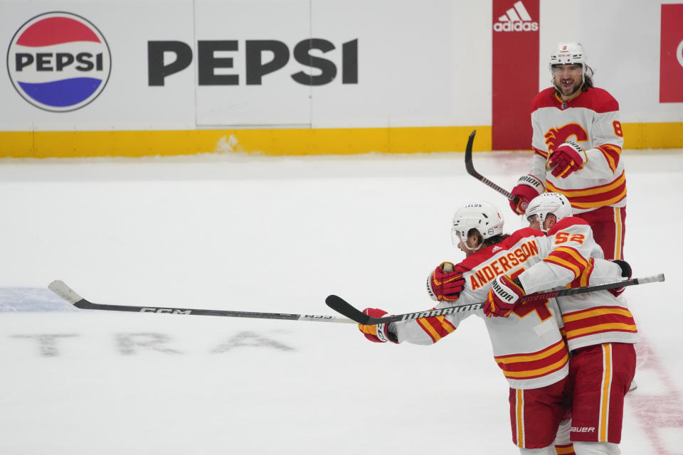 Calgary Flames defenseman Rasmus Andersson (4) celebrates scoring the winning goal during overtime against the Seattle Kraken with teammates defenseman MacKenzie Weegar (52) and defenseman Chris Tanev (8) after an NHL hockey game Monday, Nov. 20, 2023, in Seattle. The Flames won 4-3 in overtime. (AP Photo/Lindsey Wasson)