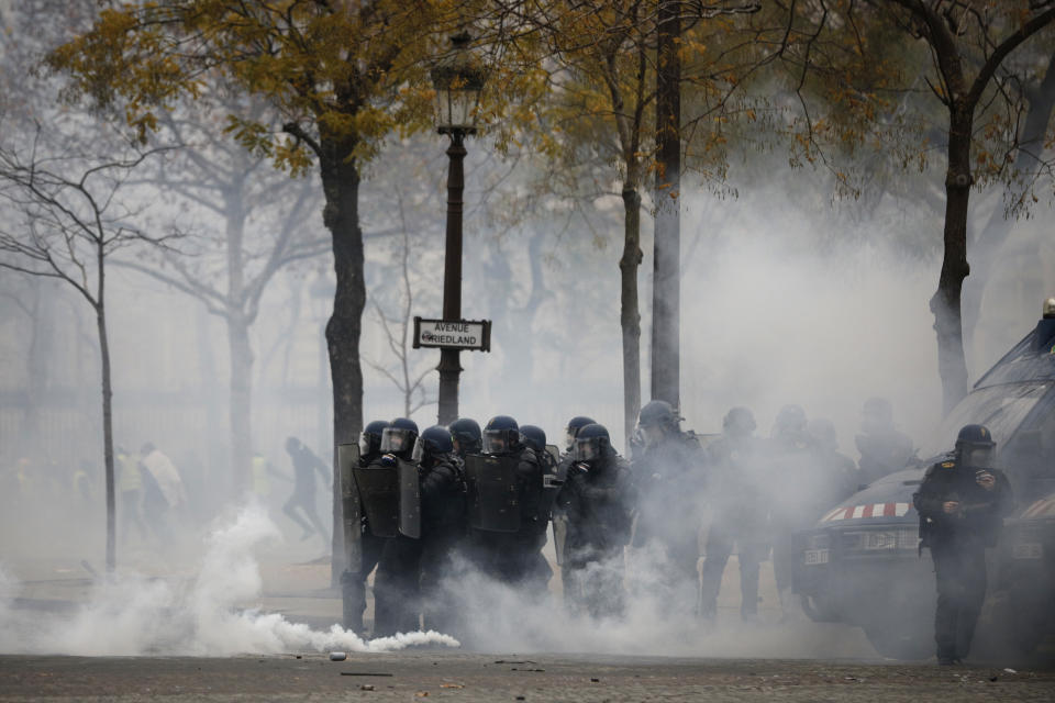 French riot police officers take position amid tear gas during a demonstration Saturday, Dec. 1, 2018 in Paris. French authorities have deployed thousands of police on Paris' Champs-Elysees avenue to try to contain protests by people angry over rising taxes and Emmanuel Macron's presidency. (AP Photo/Kamil Zihnioglu)