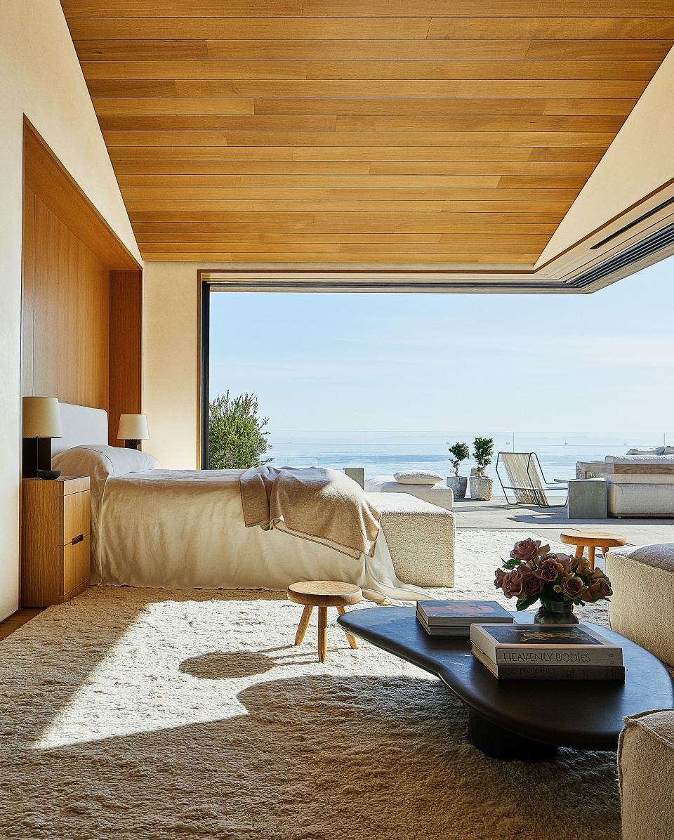 In a bedroom, Jean-Michel Frank lamps sit atop custom bedside tables. The bespoke linens are made of a Lee Jofa fabric. Charlotte Perriand stools; Axel Vervoordt cocktail table.