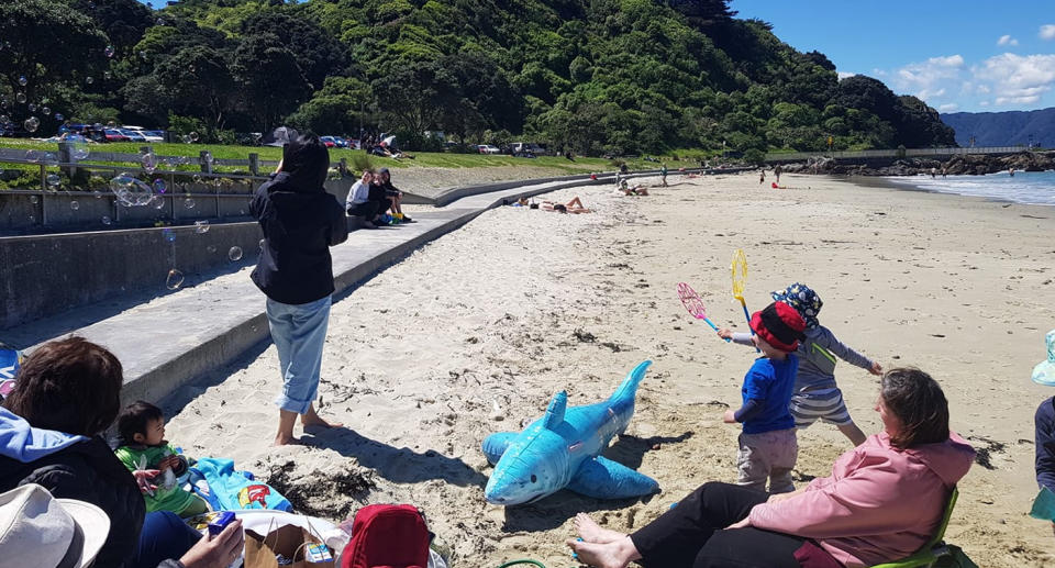 Community members brought bubbles and an inflatable shark as children run between parents sitting on chairs in the sand. 