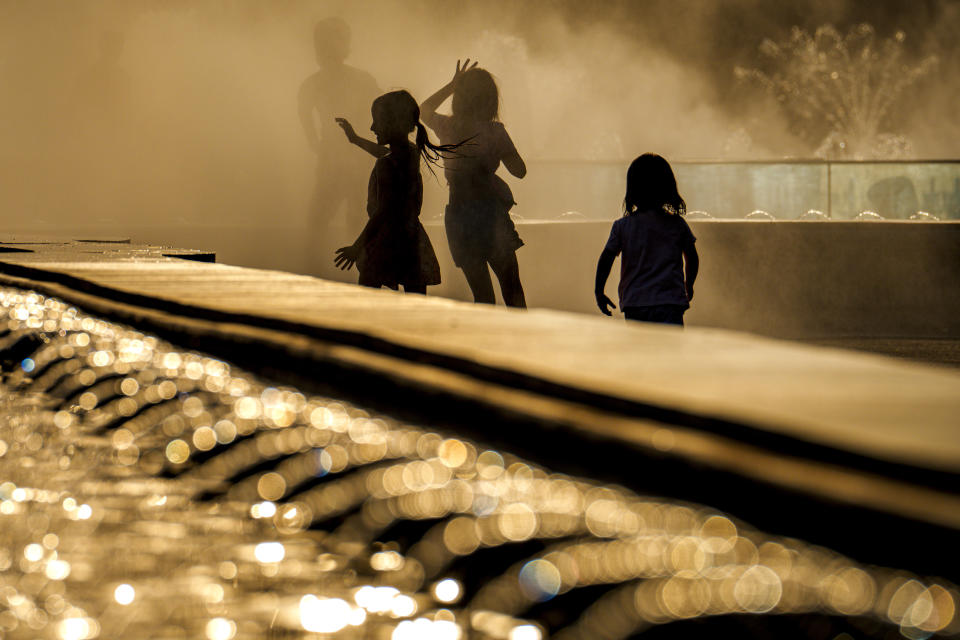 Children enjoy the drizzle from a public fountain before sunset in Bucharest, Romania, Thursday, June 20, 2024 as temperatures exceeded 38 degrees Celsius (100.4 Fahrenheit). The national weather forecaster issued a orange warning for western and southern Romania where temperatures are expected to reach 38 degrees Celsius (100.4 Fahrenheit) in the coming days. (AP Photo/Vadim Ghirda)