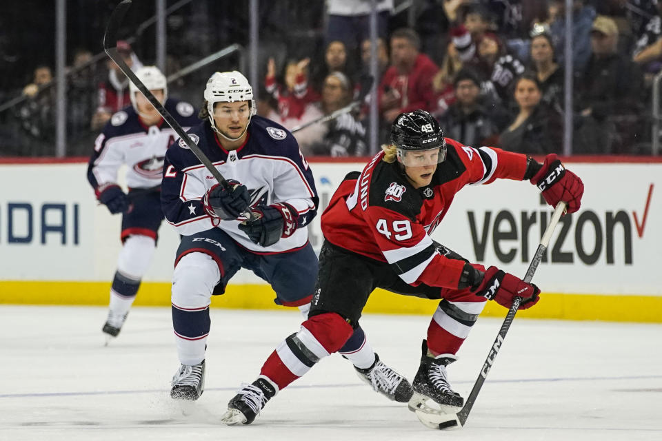 New Jersey Devils left wing Fabian Zetterlund (49) skates up ice with the puck around Columbus Blue Jackets defenseman Andrew Peeke during the first period of an NHL hockey game, Sunday, Oct. 30, 2022, in Newark, N.J. (AP Photo/Eduardo Munoz Alvarez)