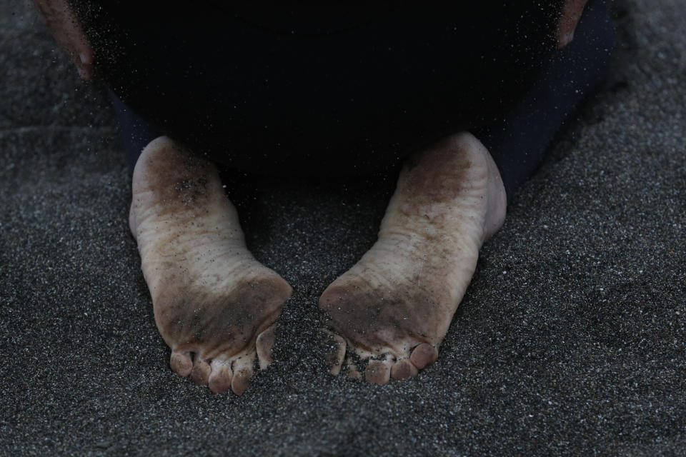 Miguel Freire, 61, who started surfing when he was 15, dusts fine gravel off his hands as he stretches before beginning his morning surf session in Lima, Peru, Friday, July 26, 2019. In the Peruvian capital, where dozens of schools teach locals and tourists from around the world how to ride the waves at beaches with Hawaiian names, professional surfers from across the Americas are preparing to compete when the sport is featured for the first time in the Pan Am Games.(AP Photo/Rebecca Blackwell)