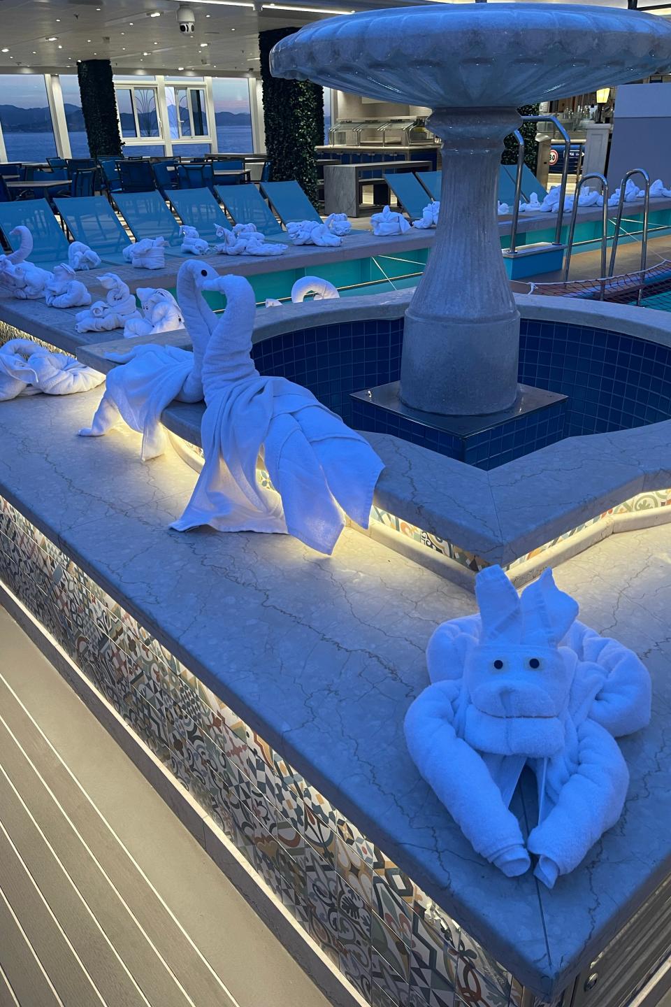 Towel animals displayed around a cruise ship pool with a fountain centerpiece