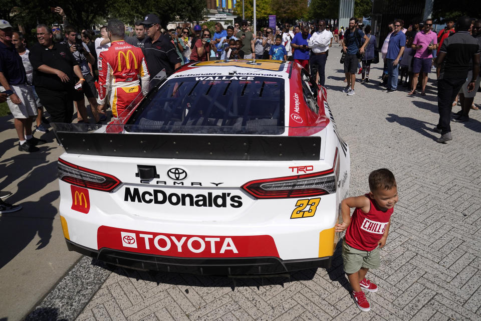 Two-year-old Brooks Elmendorf, from Dallas, touches a car as Bubba Wallace, back to camera, stands on the other side of it at Navy Pier on Tuesday, July 19, 2022, in Chicago, during a promotion for a Cup Series street race to be held in the city, July 2, 2023. (AP Photo/Charles Rex Arbogast)