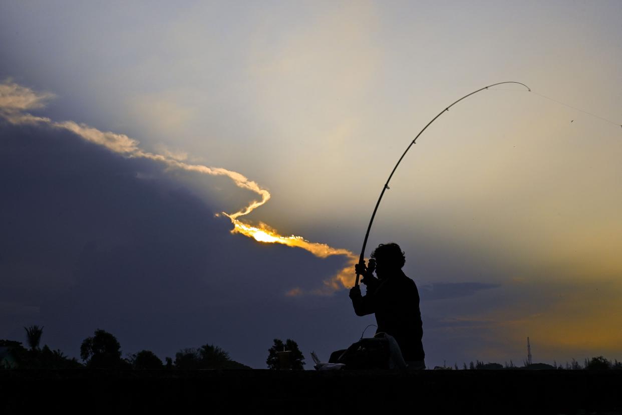 An angler casts his fishing rod at sunrise.