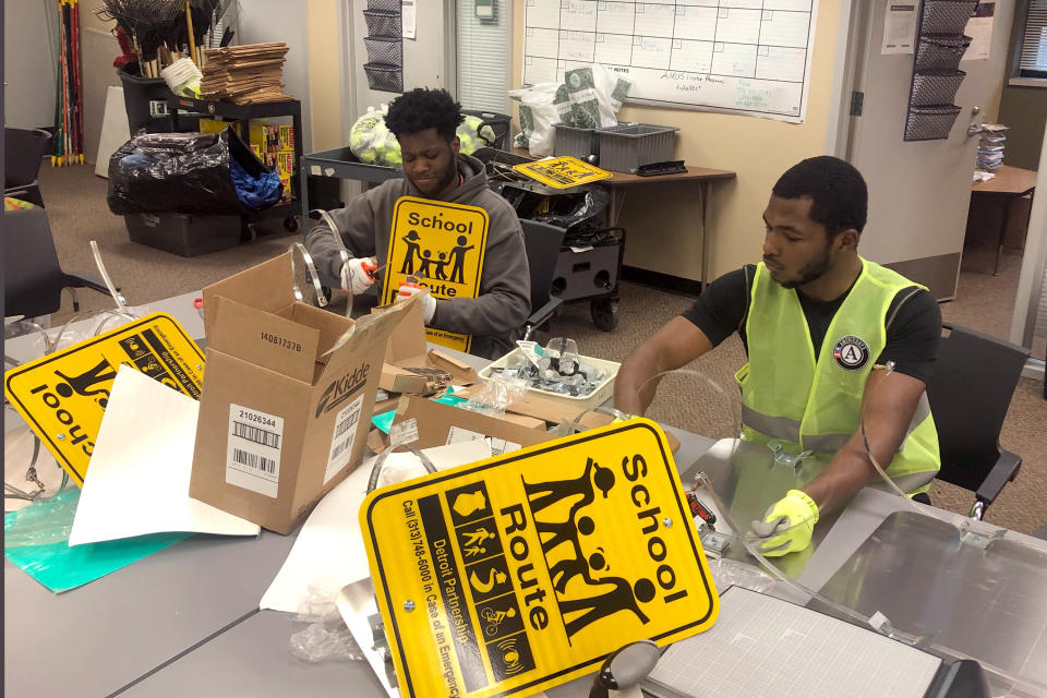 In this Jan. 16, 2020 photo, Nicholas Thomas, left, and Joe Wright, right, prepare school safety signs as part of the AmeriCorps Urban Safety Program at Wayne State University's Center for Urban Studies. Volunteers will post the signs and also help board up vacant houses Monday near a Detroit school as part of an annual project commemorating the Rev. Martin Luther King Jr's birthday and the federal holiday. (AP Photo/Corey Williams)