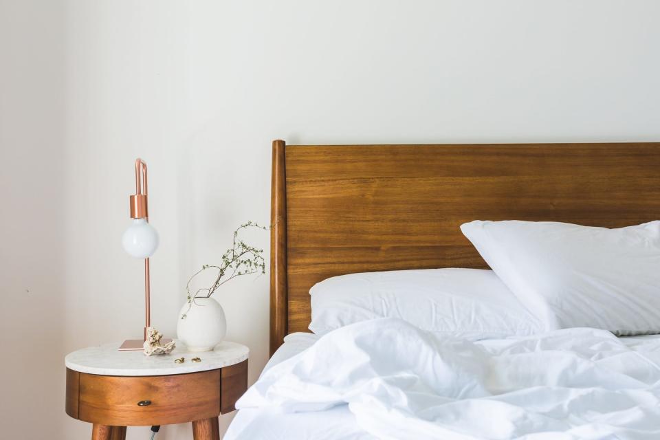 Wooden nightstand next to wooden headboard and white bed