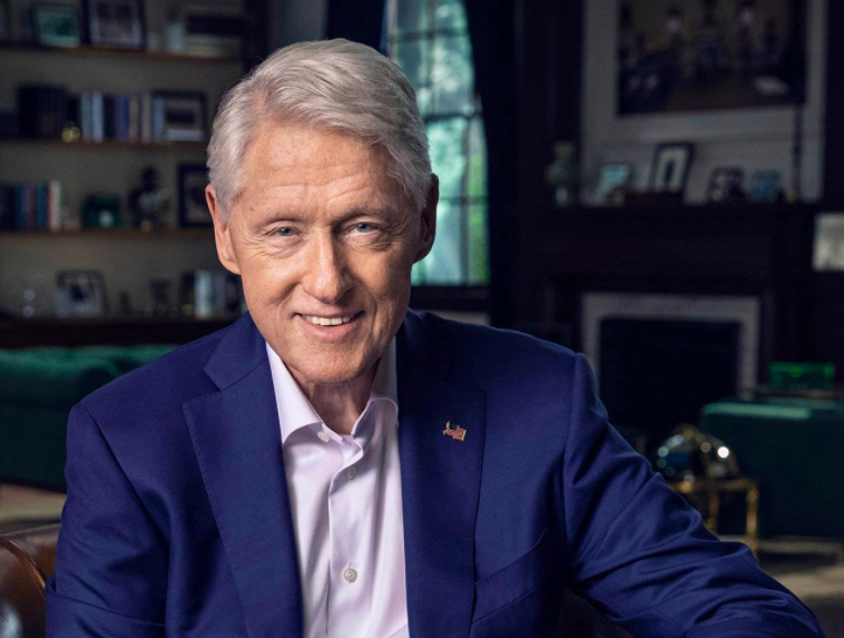 Bill Clinton in a blue jacket, smiling. 