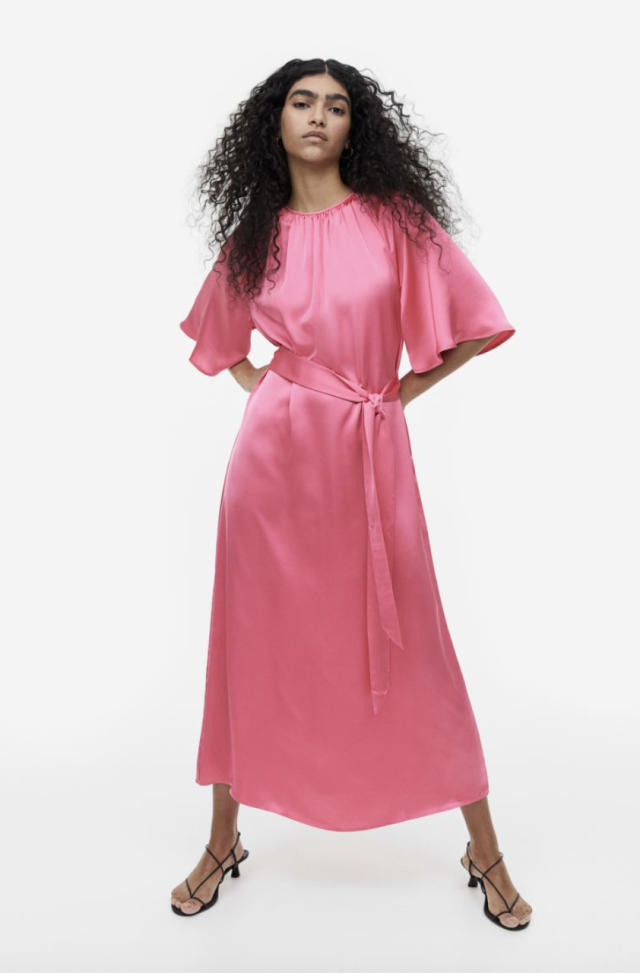model with long black curly hair wearing pink shiny dress belted with flutter sleeves maxi dress, Tie-Belt Satin Dress (Photo via H&M)