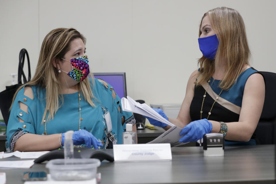 Miami-Dade County Judge Victoria Ferrer, left, and Supervisor of Elections Christina White, right examine signatures on vote-by-mail ballots for the August 18 primary election as the canvassing board meets at the Miami-Dade County Elections Department, Thursday, July 30, 2020, in Doral, Fla. President Donald Trump is for the first time publicly floating a "delay" to the Nov. 3 presidential election, as he makes unsubstantiated allegations that increased mail-in voting will result in fraud. (AP Photo/Lynne Sladky)