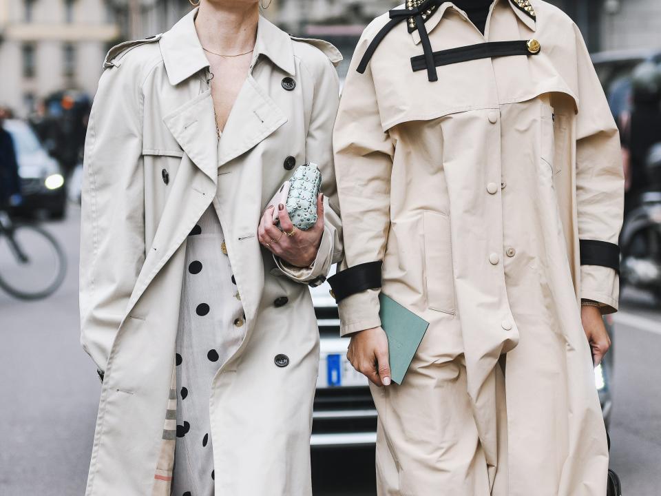 two people walking down the street wearing tan trench coats and sunglasses