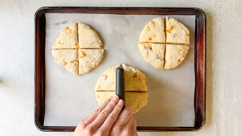 Scoring peaches and cream scone dough into quarters with dough divider on baking sheet