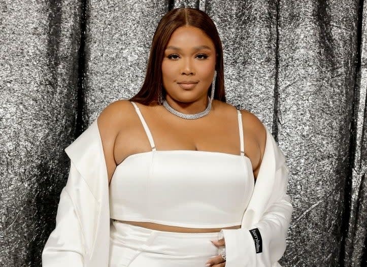 Lizzo poses in a white, off-the-shoulder outfit with ruffles, accessorized with a choker