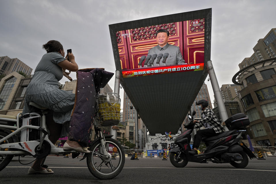 A woman on her electric-powered scooter films a large video screen outside a shopping mall showing Chinese President Xi Jinping speaking during an event to commemorate the 100th anniversary of China's Communist Party at Tiananmen Square in Beijing, Thursday, July 1, 2021.(AP Photo/Andy Wong)