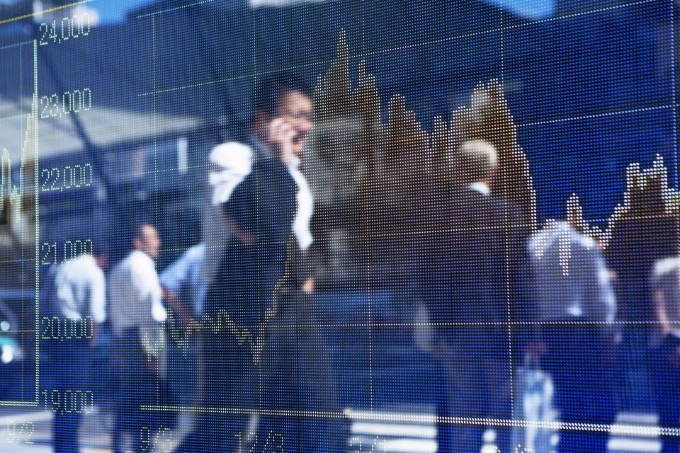 A silhouette of business man  talking on smart phone and walking on the road is reflected on the display of the stock price chart in the business district.