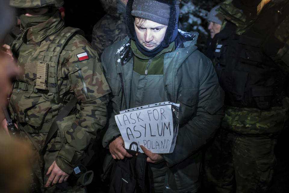 FILE - An asylum seeker from Syria who has been taken into custody by Polish border guards holds a paper saying "I ask for asylum in Poland," in Harkawicze, Poland, Dec. 1, 2021. A year after migrants started crossing into the European Union from Belarus to Poland, Polish authorities are planning to announce Thursday that a 5.5-meter-tall steel wall along its border to the north with Belarus is set to be completed. The purpose of the wall is to keep out asylum seekers fleeing conflict and poverty in the Middle East and Africa. (AP Photo/Michal Kosci, File)