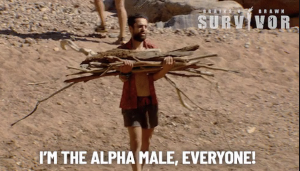 Man carrying sticks on "Survivor" with caption "I'M THE ALPHA MALE, EVERYONE!"