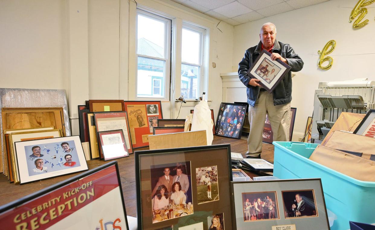 Former Tangier owner Ed George holds a photo of Dick and Tom Smothers, better known as the Smothers Brothers, while looking through stacks of autographed photos, posters and other memorabilia from entertainers who came to Akron.