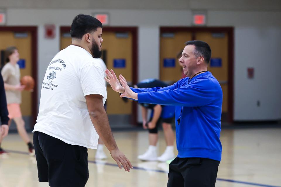 Winnacunnet High School boys basketball head coach Jay McKenna, right, demonstrates body position with assistant coach Seth Provencher during Tuesday's practice.