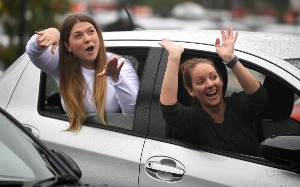 Two women react as they watch Australian singer Casey Donovan's live performance from their car during a drive-in concert  - EPA