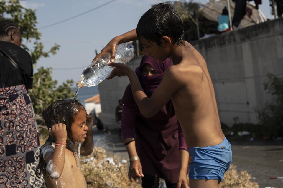 A boy uses a bottle of water to wash a girl as migrants gather near Mytilene town, on the northeastern island of Lesbos, Greece, Saturday, Sept. 12, 2020. Greek authorities have been scrambling to find a way to house more than 12,000 people left in need of emergency shelter on the island after the fires deliberately set on Tuesday and Wednesday night gutted the Moria refugee camp. (AP Photo/Petros Giannakouris)