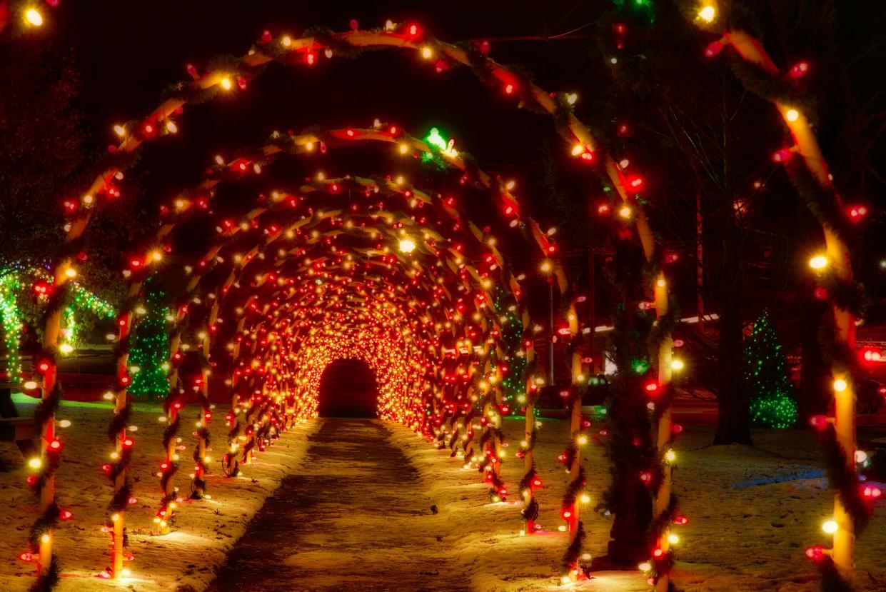A tunnel of festively lighted Christmas arches decorates a walkway on a small town public square