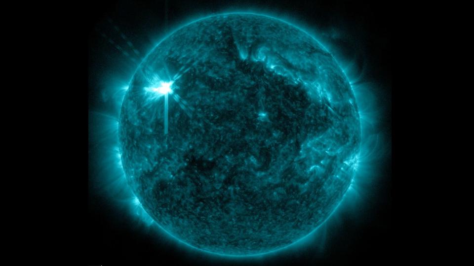 a false-color photograph of the sun showing a bright white spot in its upper-left quadrant