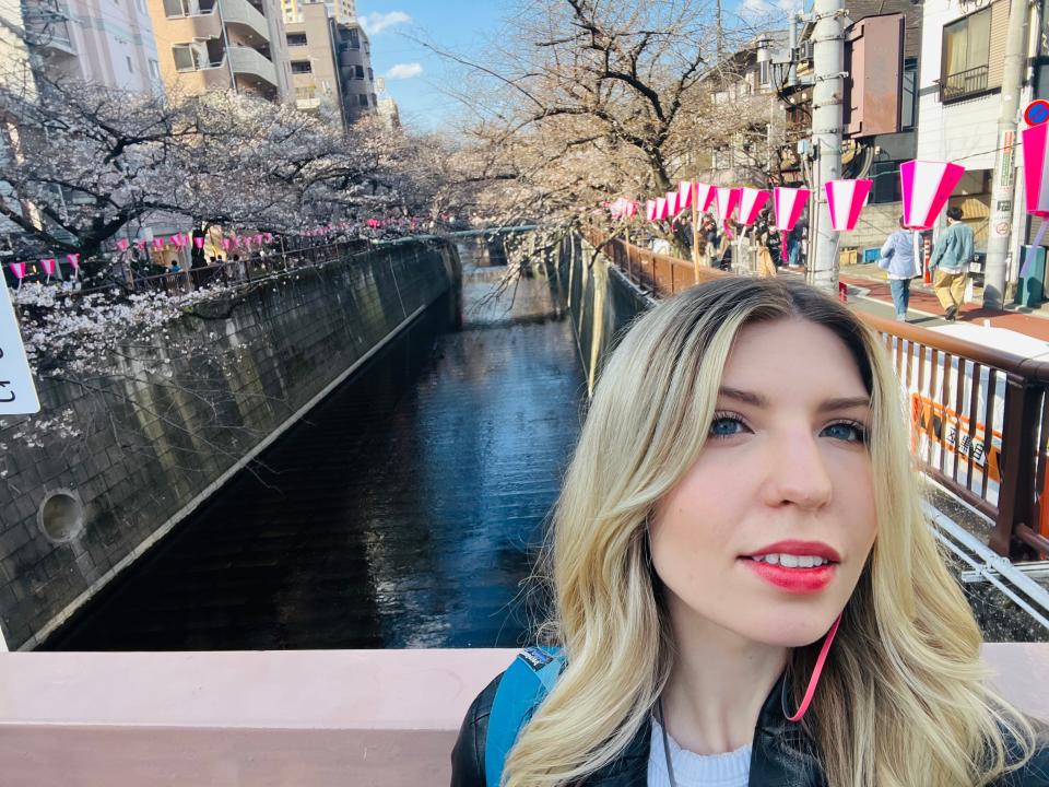 abi posing on a bridge over a river in japan during cherry blossom season