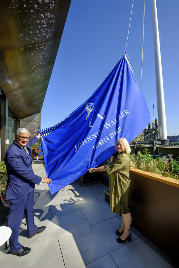 Ivan Menezes, Chief Executive, Diageo, and Barbara Smith, Managing Director of Johnnie Walker Princes Street, raise a Johnnie Walker flag to mark the opening of Johnnie Walker Princes Street set against the backdrop of Edinburgh’s iconic skyline, including the world-famous Edinburgh Castle.