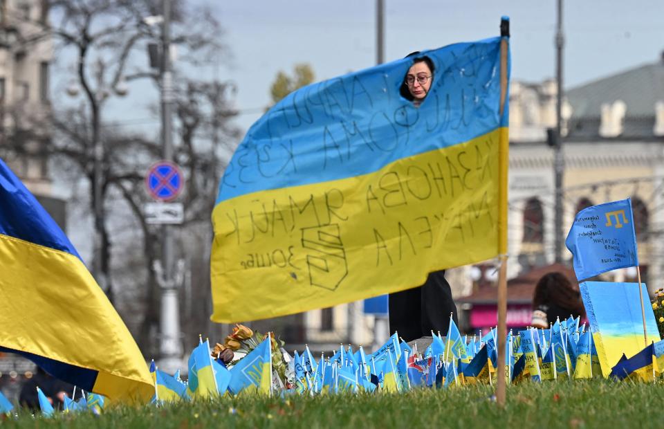 A woman seen through a hole in a Ukrainian flag mourns at a makeshift memorial for fallen soldiers at Independence Square in Kyiv, (AFP via Getty Images)