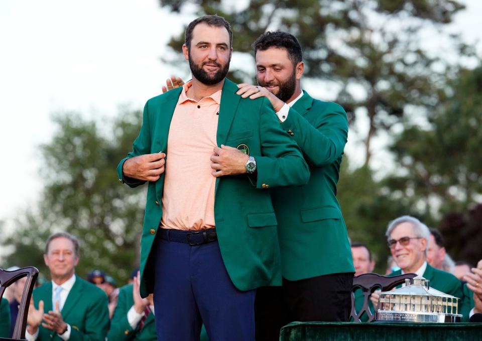 Scottie Scheffler puts on his green jacket with some assistance from 2023 Masters champion Jon Rahm on Sunday evening.
