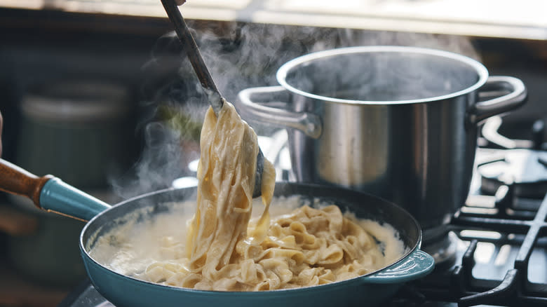 adding pasta to alfredo sauce on the stove