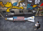 In this June 29, 2019, photo, shoppers walk past a bench shaped like a missile painted with the U.S. flag outside of a clothing store at a shopping mall in Beijing. U.S. President Donald Trump angrily escalated his trade fight with China on Friday, Aug. 23, 2019, raising retaliatory tariffs and ordering American companies to consider alternatives to doing business there. (AP Photo/Mark Schiefelbein)