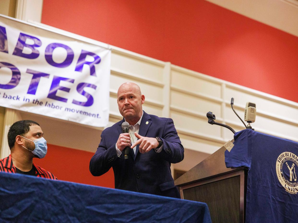 A man in a suit speak in front of a lecturn and a sign that reads "labor votes."