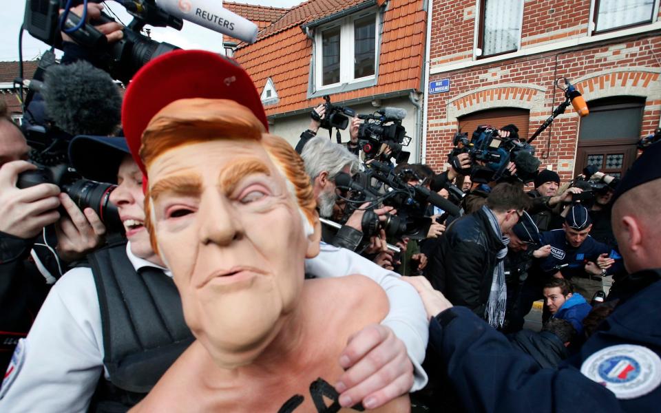 A Femen activist wearing the mask of U.S President Donald Trump is detained as she demonstrates in Henin-Beaumont, northern France, where far-right leader and presidential candidate Marine Le Pen was voting - Credit: Michel Spingler /AP