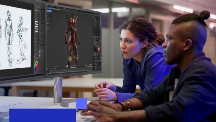 A woman and a man sit together by a desk, using a graphics editing program on a computer.