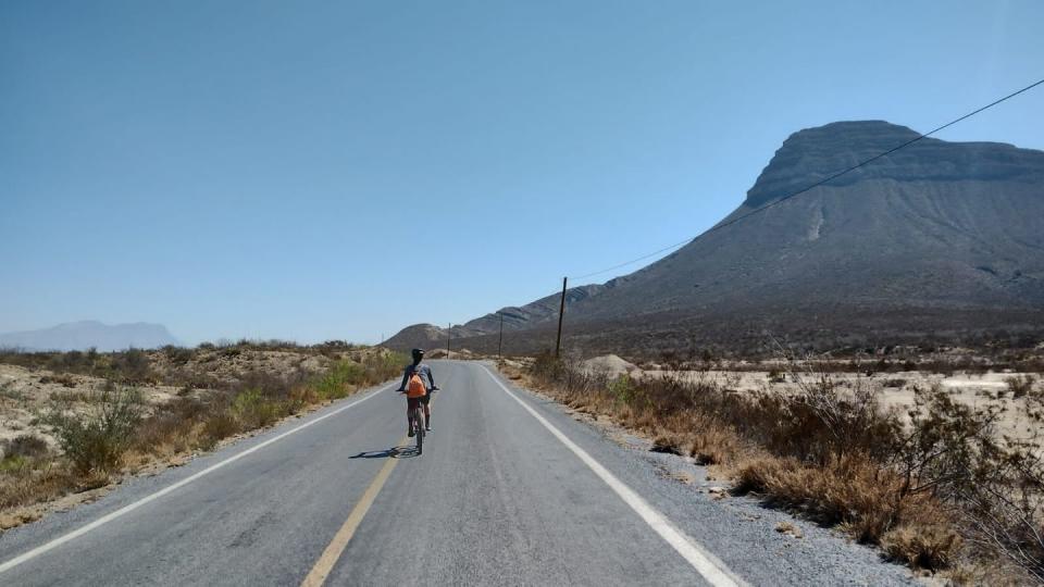 a person riding a bicycle on a road with mountains in the background