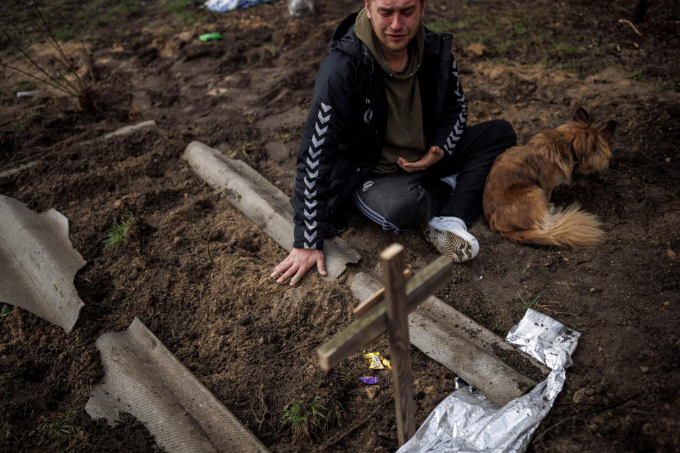 Serhii Lahovskyi sits on the ground next to the grave of his friend.