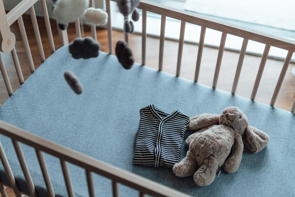 A striped baby outfit and a plush teddy bear placed in an empty crib with a mobile hanging above