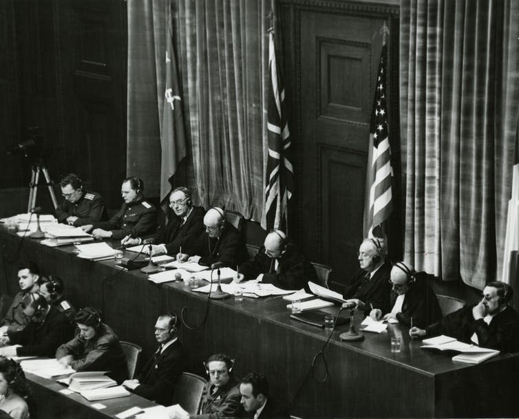 <span class="caption">The Nuremberg judges panel, backed by the US, UK and USSR flags.</span> <span class="attribution"><a class="link " href="https://commons.wikimedia.org/wiki/File:View_of_judges_panel_during_testimony_Nuremberg_Trials_1945.jpeg" rel="nofollow noopener" target="_blank" data-ylk="slk:Wikimedia Commons;elm:context_link;itc:0;sec:content-canvas">Wikimedia Commons</a></span>