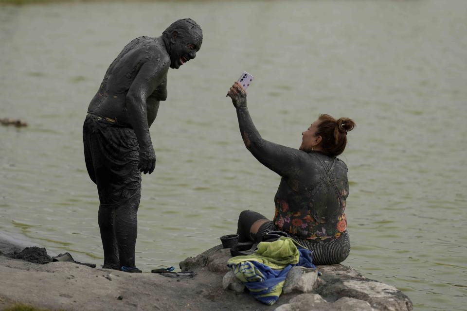 Cubiertos en un lodo oscuro de los pies a la cabeza, Manuel Hernández y su esposa Josefina se ríen en la orilla de la laguna Las Salinas, en Chilca, Perú, el 3 de febrero de 2024. Las Salinas es una laguna rica en sal y otros minerales. (AP Foto/Martín Mejía)