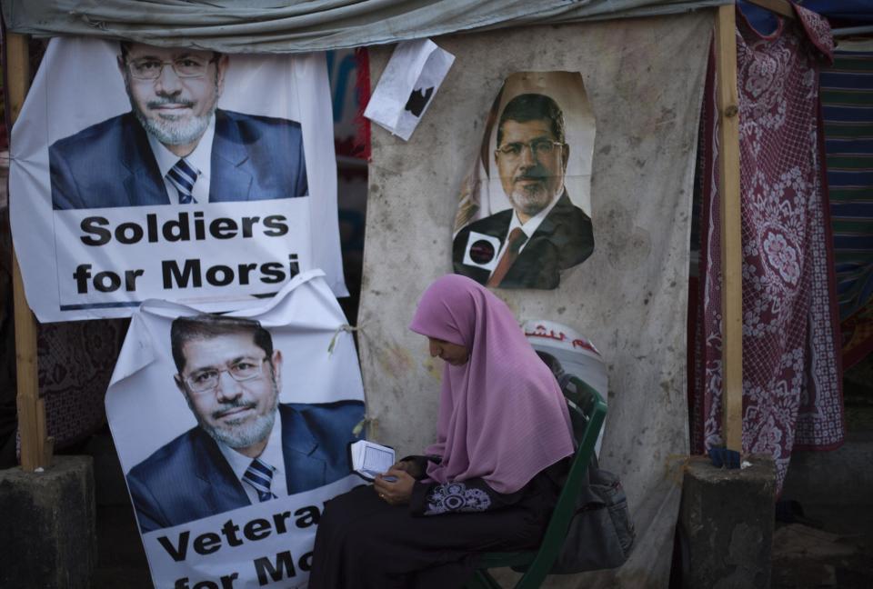 FILE - In this Thursday, Aug. 1, 2013 file photo, A supporter of Egypt's ousted President Mohammed Morsi reads the Muslim's holy book Quran as she sits next to a tent with posters of Morsi outside Rabaah al-Adawiya mosque, where protesters have installed a camp and hold daily rallies at Nasr City in Cairo, Egypt. Egyptian officials say security authorities leaked a recording of a private conversation between ousted President Mohammed Morsi and his lawyer on the sidelines of his trial, in which Morsi says protests by his supporters and the crackdown on them are "useless." (AP Photo/Khalil Hamra)